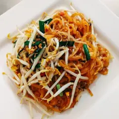 Pad Thai z kiełkami fasoli mung, jajkiem i szczypiorkiem na białym talerzu.