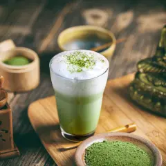 Szklanka zielonej herbaty matcha z pianką, obok naczynia z proszkiem matcha i bambusowe akcesoria.
