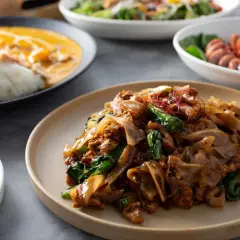 Talerz z makaronem ryżowym, mięsem i zielonymi warzywami, ozdobiony chili.