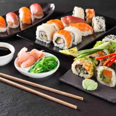 Różnorodne sushi, sos sojowy, marynowany imbir, sałatka wakame i pałeczki na ciemnym tle.