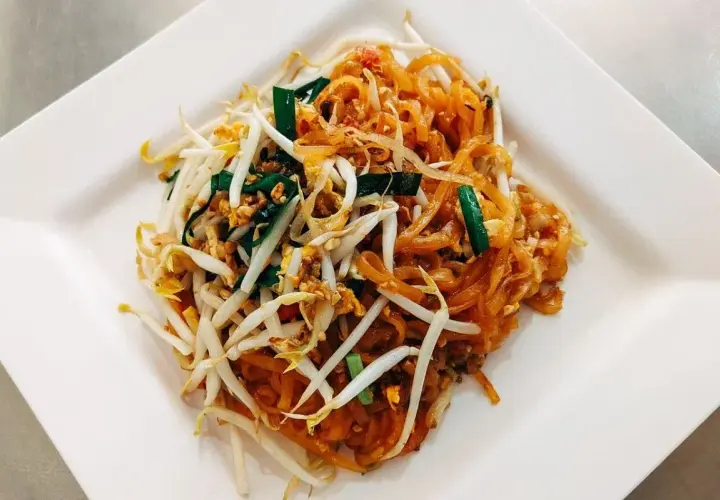 Pad Thai z kiełkami fasoli mung, jajkiem i szczypiorkiem na białym talerzu.