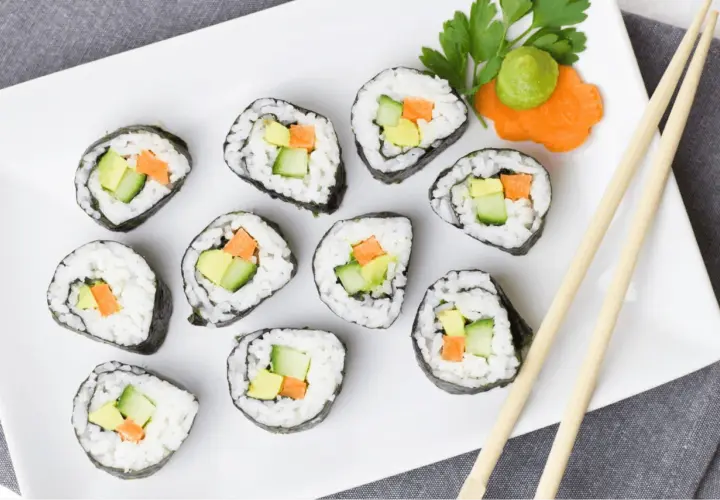 Talerz z sushi z awokado, ogórkiem i marchewką, pałeczki i wasabi.