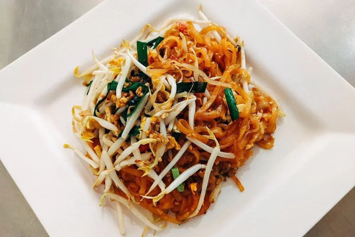 Pad Thai z kiełkami fasoli mung, jajkiem i szczypiorkiem na białym talerzu.