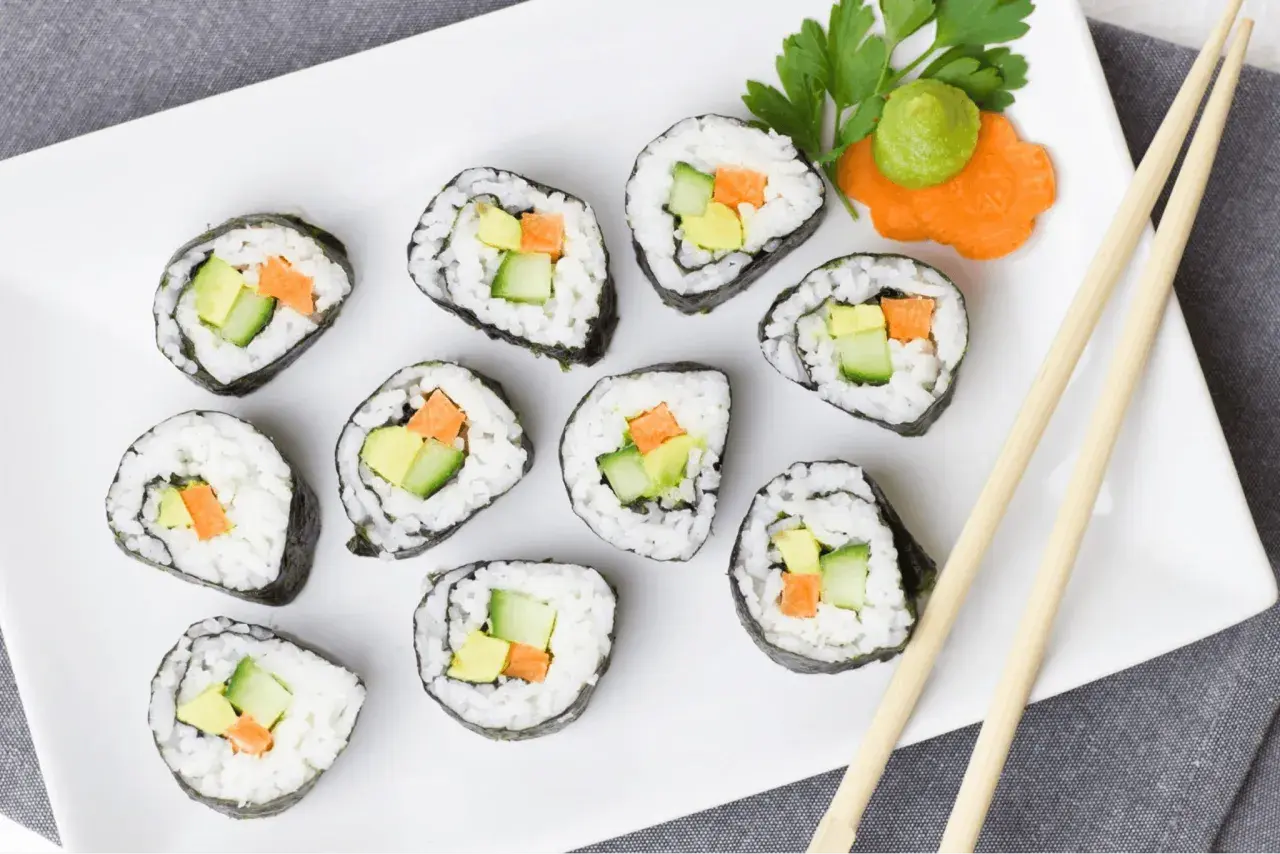 Talerz z sushi z awokado, ogórkiem i marchewką, pałeczki i wasabi.