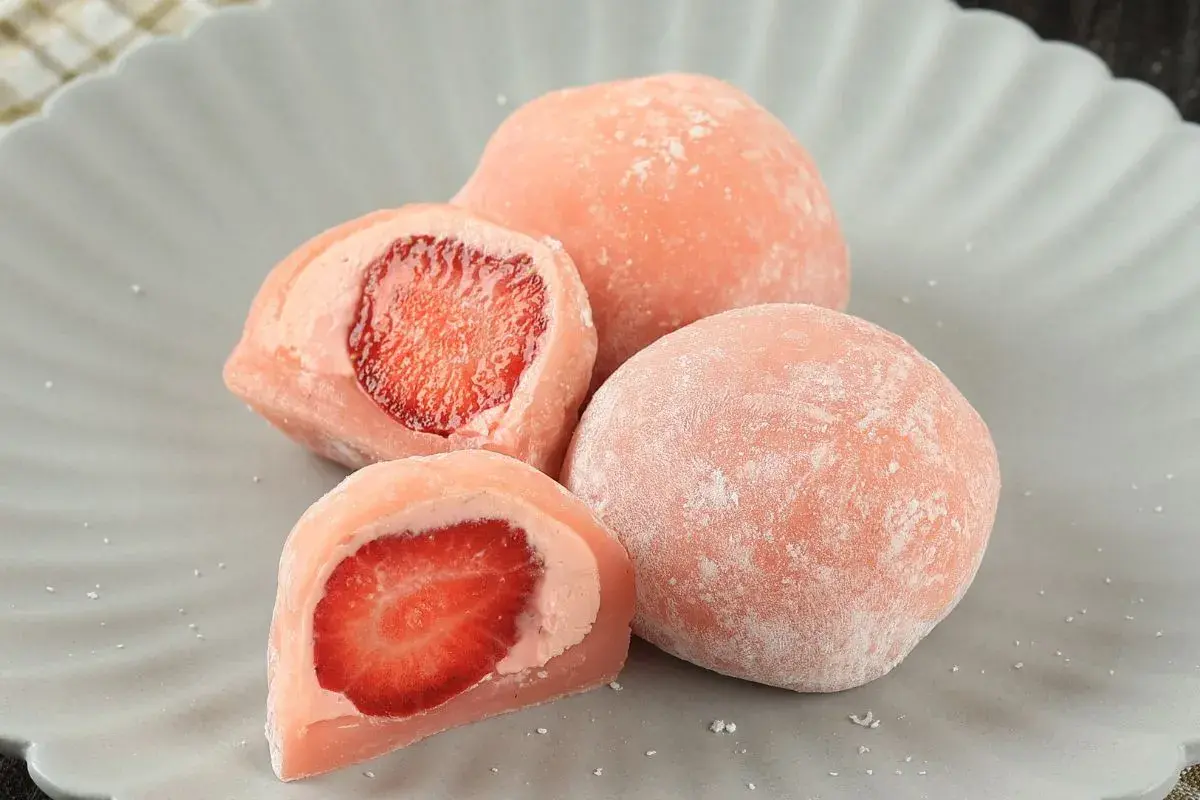 Różowe mochi z truskawkami na szarym talerzu.